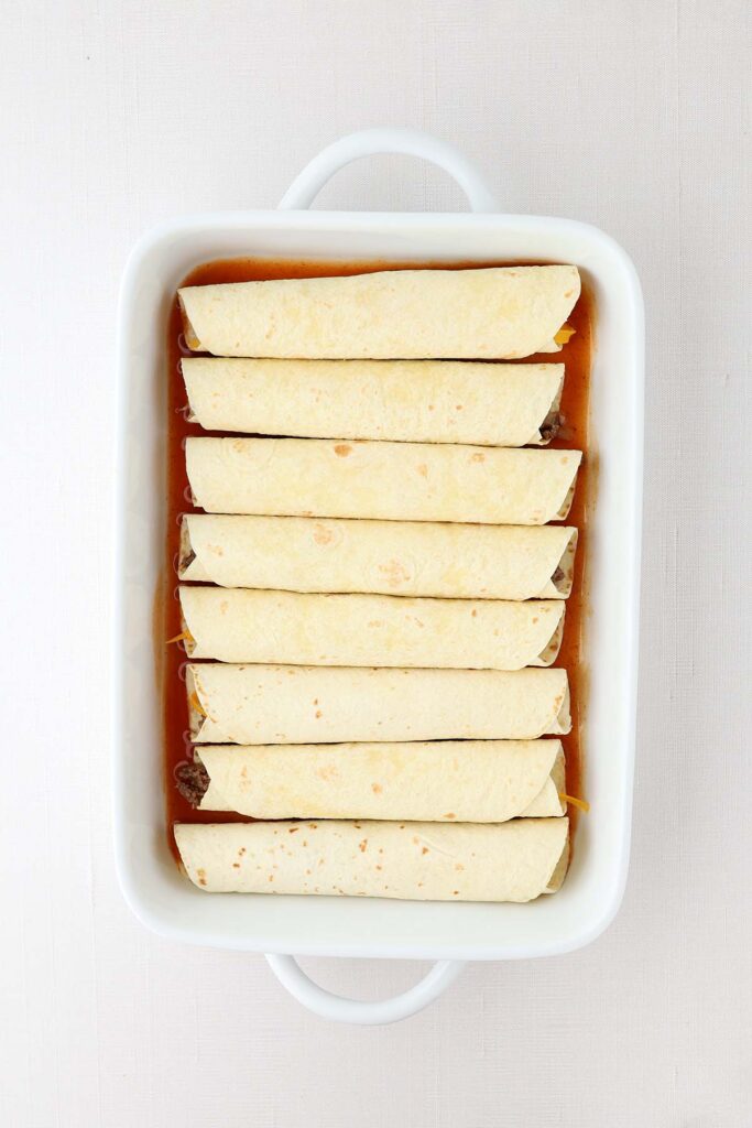 top down image showing a white baking dish filled with enchiladas with no sauce or cheese