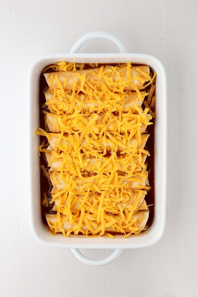top down image showing a white baking dish filled with enchiladas that have not been baked