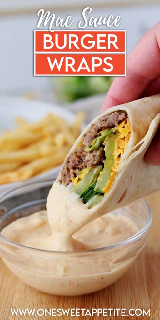 Close-up of a hand dipping a Big Mac wrap filled with ground beef, lettuce, pickles, and shredded cheese into a bowl of creamy special sauce, with French fries and fresh lettuce blurred in the background.