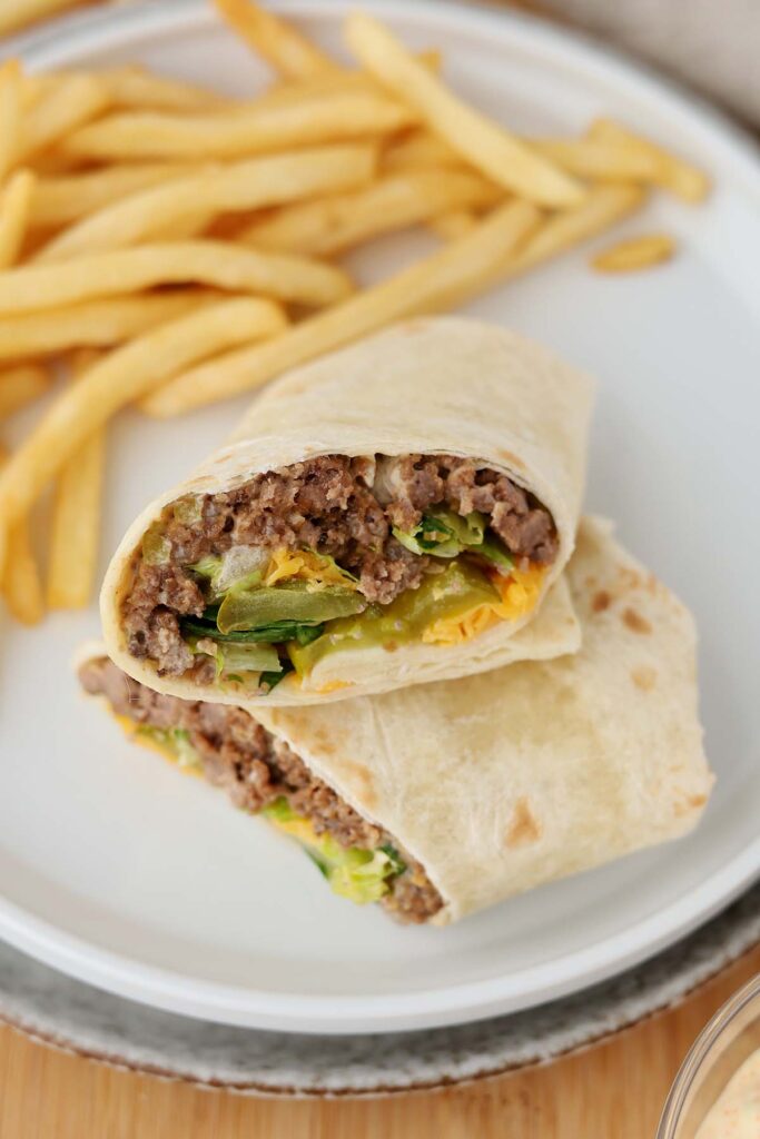 close up of a burger wrap that has been cut in half and stacked on a white plate with fries