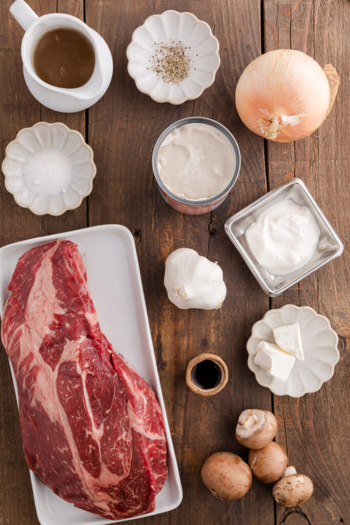 Top down image showing a chuck roast and other ingredients for beef stroganoff sitting on a wooden table top