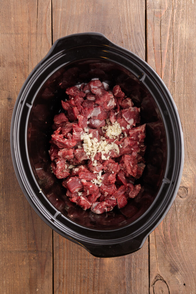 Top down image showing a crockpot with uncooked beef and seasoning