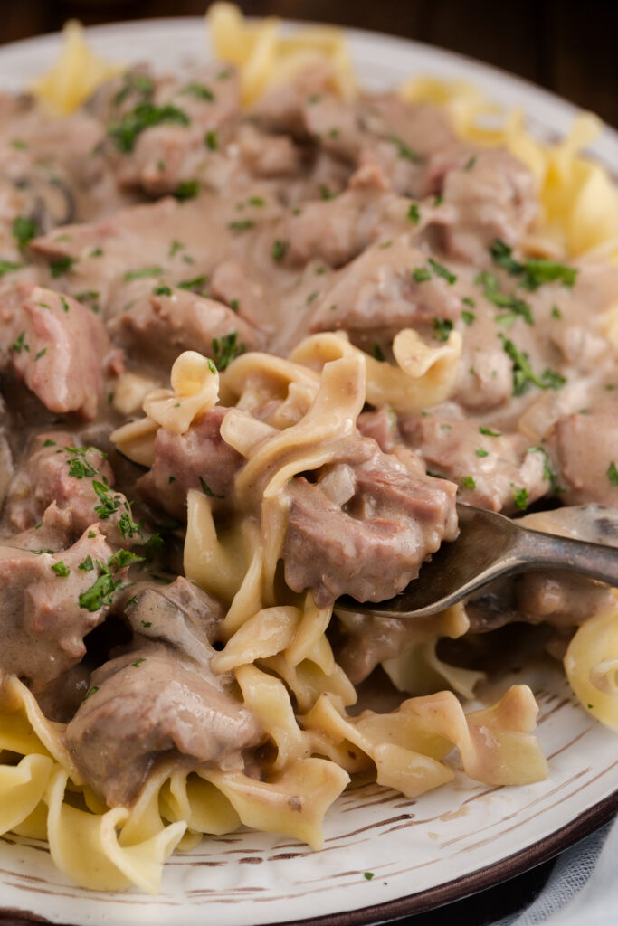 Close up image showing a plate of egg noodles with a saucy beef mix on top with a bite on a fork.