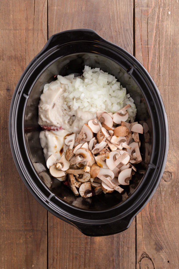 top down image howing fresh mushrooms and onions inside a slow cooker