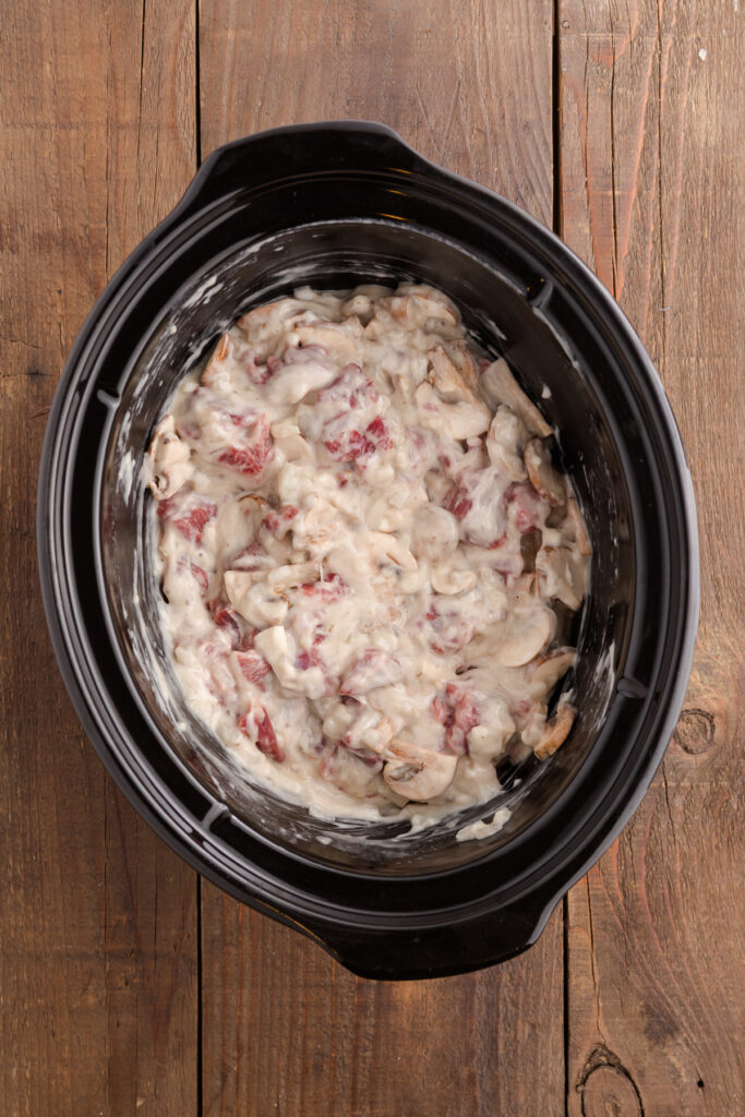 Top down image showing a creamy beef mixture inside a slow cooker