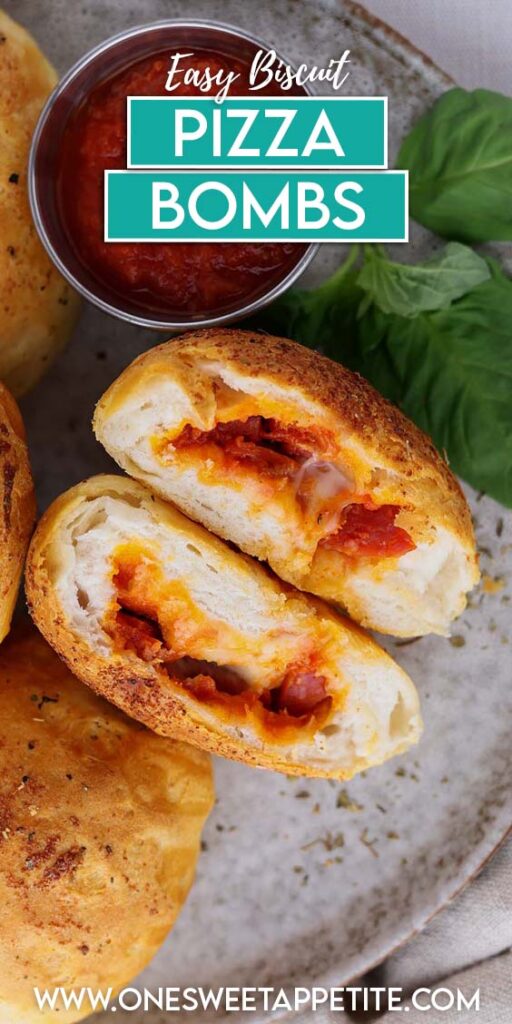top down image showing a light grey plate filled with baked biscuits. One is cut in half showing melted cheese and pepperoni. There is a container of red sauce and a sprig of basil. Text overlay reads "easy biscuit pizza bombs"