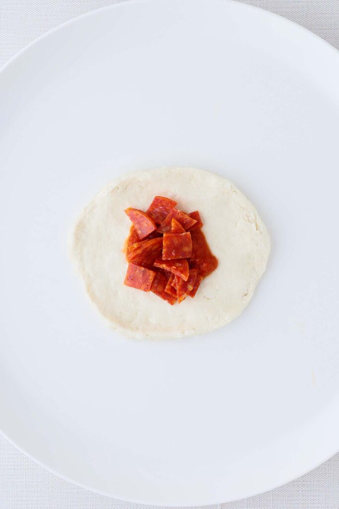 top down image showing a flattened biscuit topped with pizza sauce and pepperoni