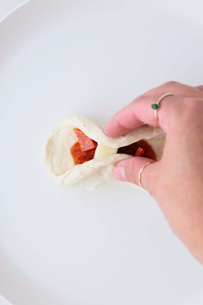 Top down image showing a biscuit with pizza toppings being pinched together on a white plate