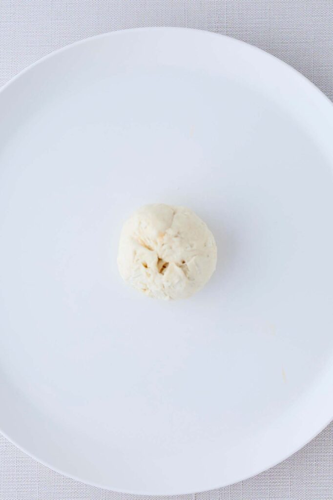 Top down image showing a pinched together biscuit ball on a white plate