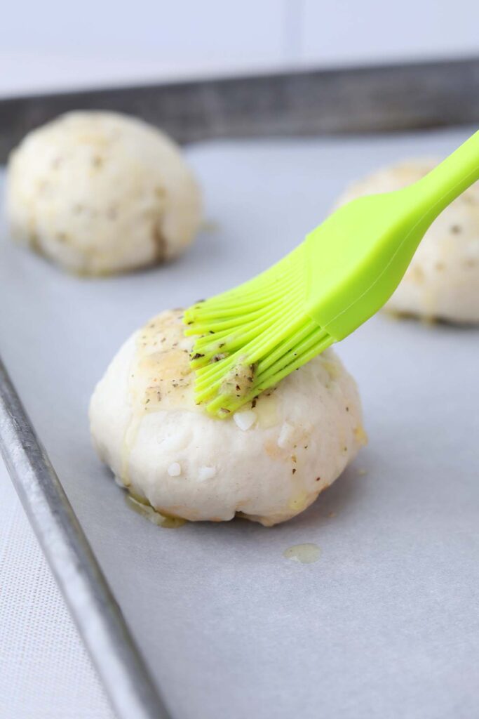 unbaked biscuit being brushed with melted butter and spices by a bright green silicone brush