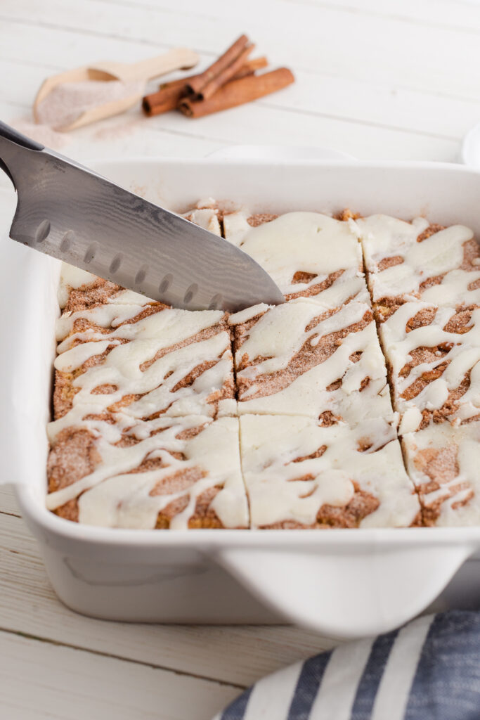 close up showing squares of blondies that are topped with a glaze being cut by a sharp knife