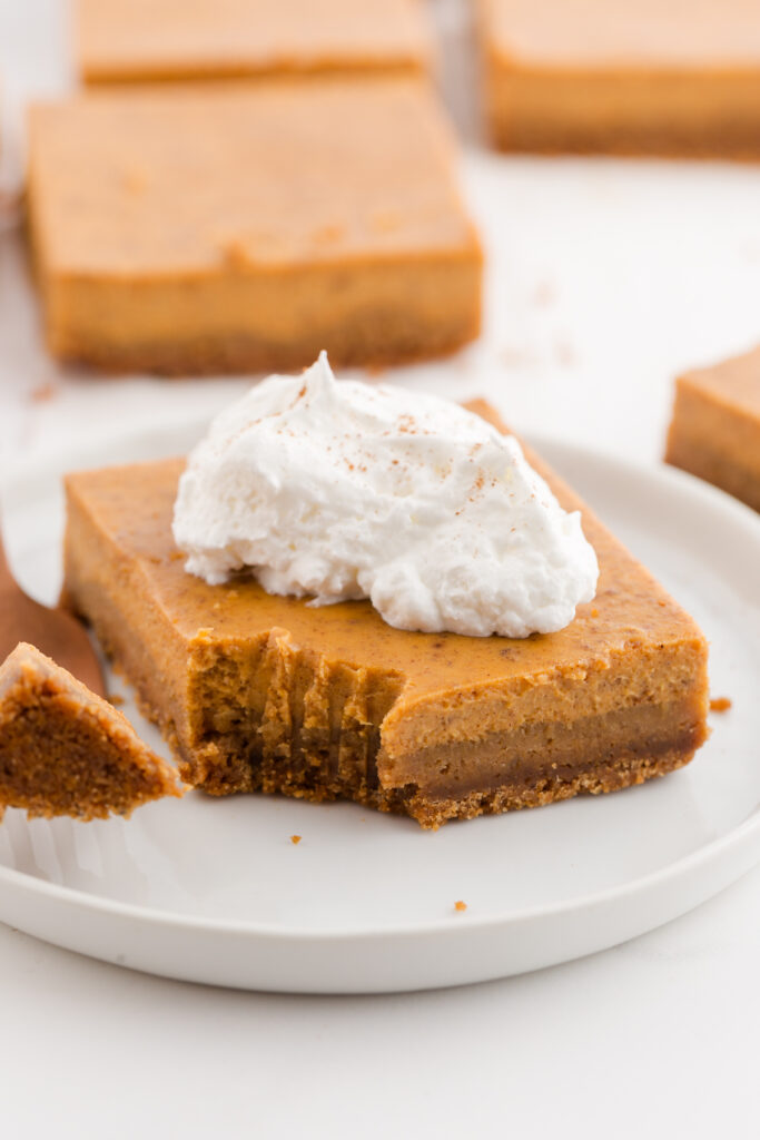 close up image showing a pie bar with whipped cream sitting on a white plate with a bite taken out of it