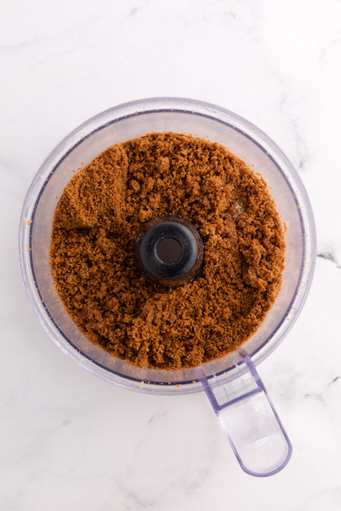 Top down image showing a food processor filled with crushed cookies and flour