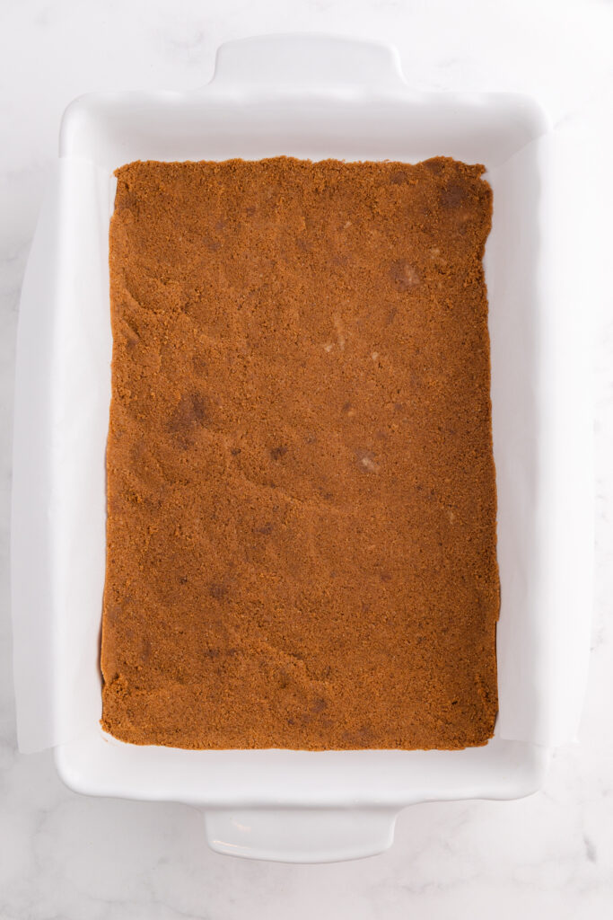 Top down image showing a white baking dish filled with graham cracker crust