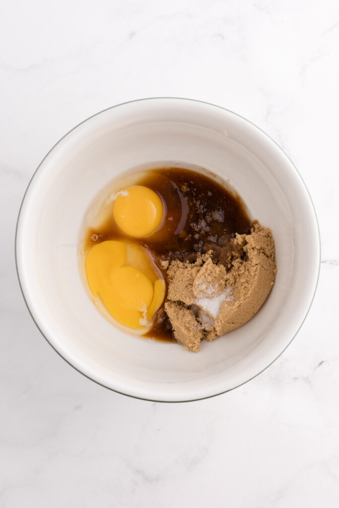Top down image showing a white bowl filled with brown sugar, vanilla, and eggs