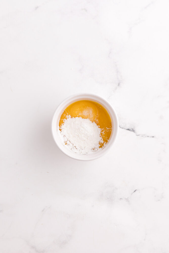 Top down image showing a small bowl filled with unmixed egg yolks and cornstarch
