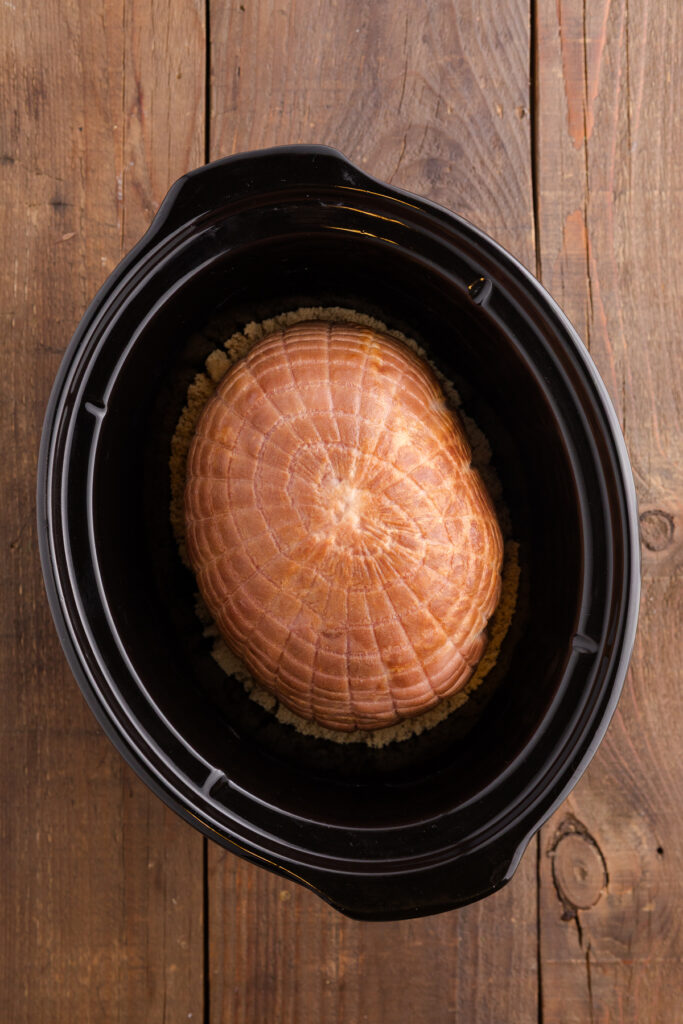 top down image showing brown sugar in a slow cooker topped with a ham