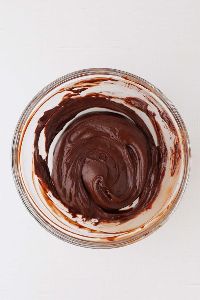 One bowl of glossy brownie cookie batter with a thick, chocolatey texture, photographed from overhead on a white background.