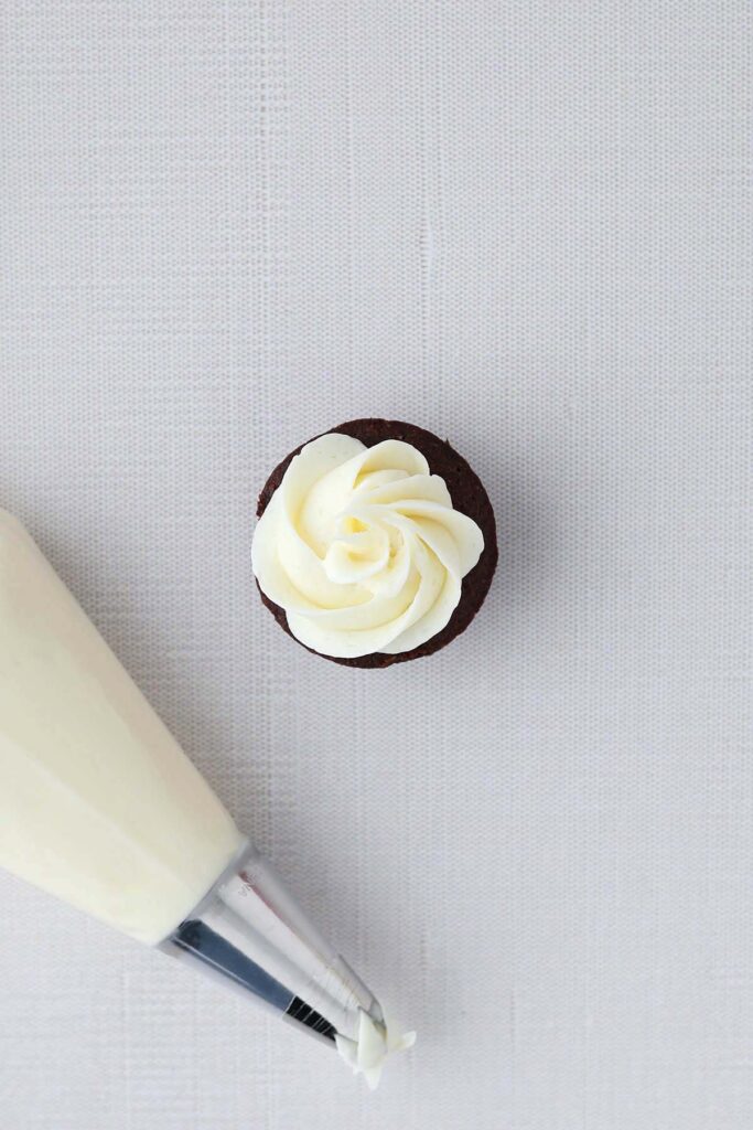 top down image showing a brownie with piped white frosting on a white table top. There is a piping bag off to the side