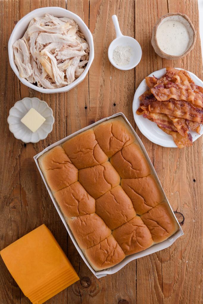 Overhead view of shredded chicken, bacon, ranch dressing, cheese, and Hawaiian rolls