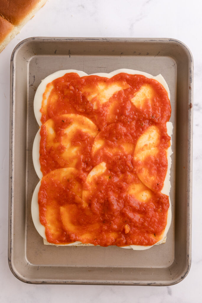 Top down image showing rolls sliced in half with cheese on top spread with red sauce