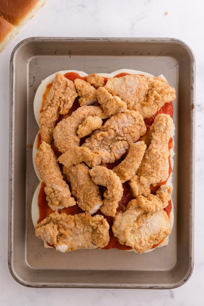 Top down image showing rolls sliced in half with cheese on top spread with red sauce and topped with chicekn strips