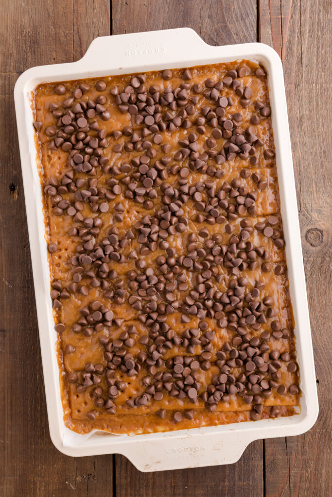 Baking sheet lined with saltine crackers arranged in a single even layer topped with toffee and sprinkled with chocolate chips