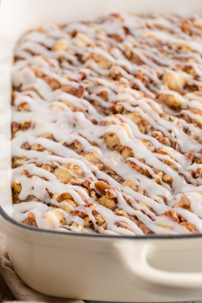 close up image showing a white 9x13 pan with a cinnamon roll bkae that is topped with a glaze 
