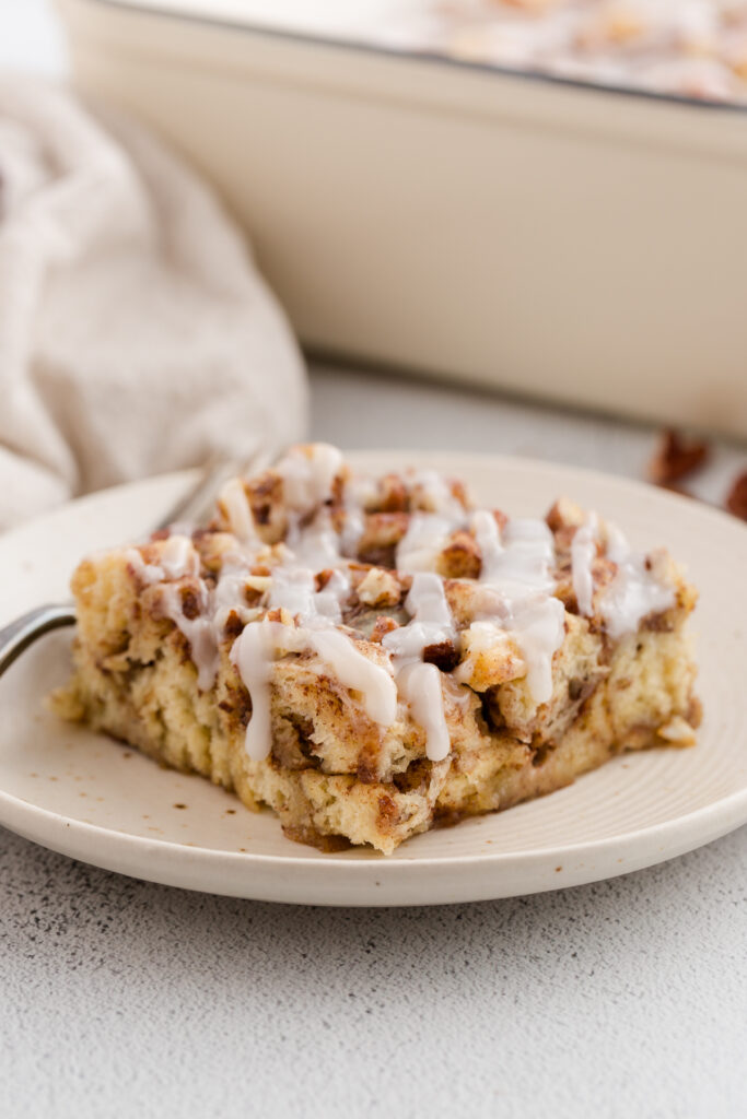 close up image showing a cut out piece of cinnamon roll bake with a glaze on top sitting on a white plate