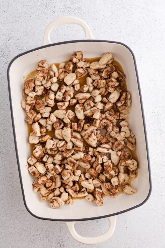 Top down image showing a 9x13 pan with a brown sugar mixture in the bottom topped with cut cinnamon rolls