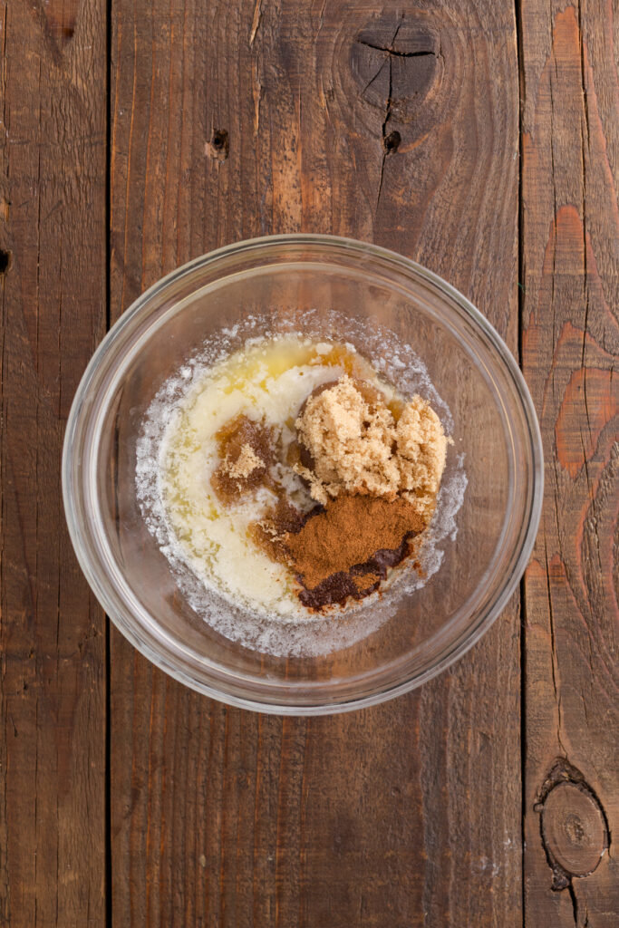 ingredients in a mixing bowl before blending, including softened cream cheese, butter, powdered sugar, brown sugar, cinnamon, and vanilla.