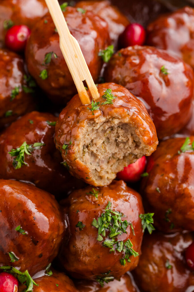 close up image showing a meatball covered in sauce being pulled up by a toothpick