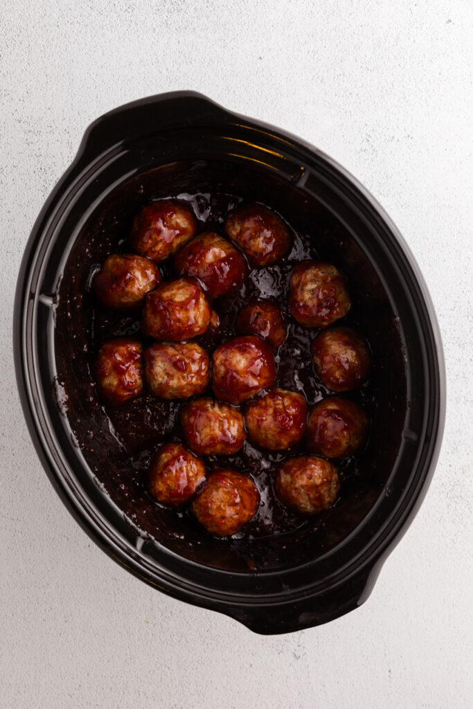 Top down image showing meatballs in a slow cooker covered in sauce