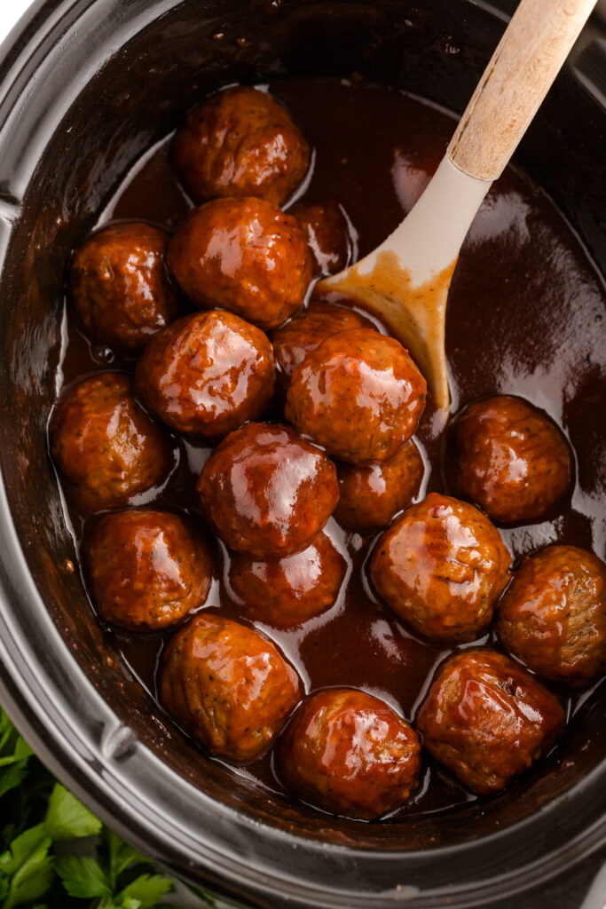 close up of the inside of a slow cooker filled with meatballs in a sauce with some being scooped out