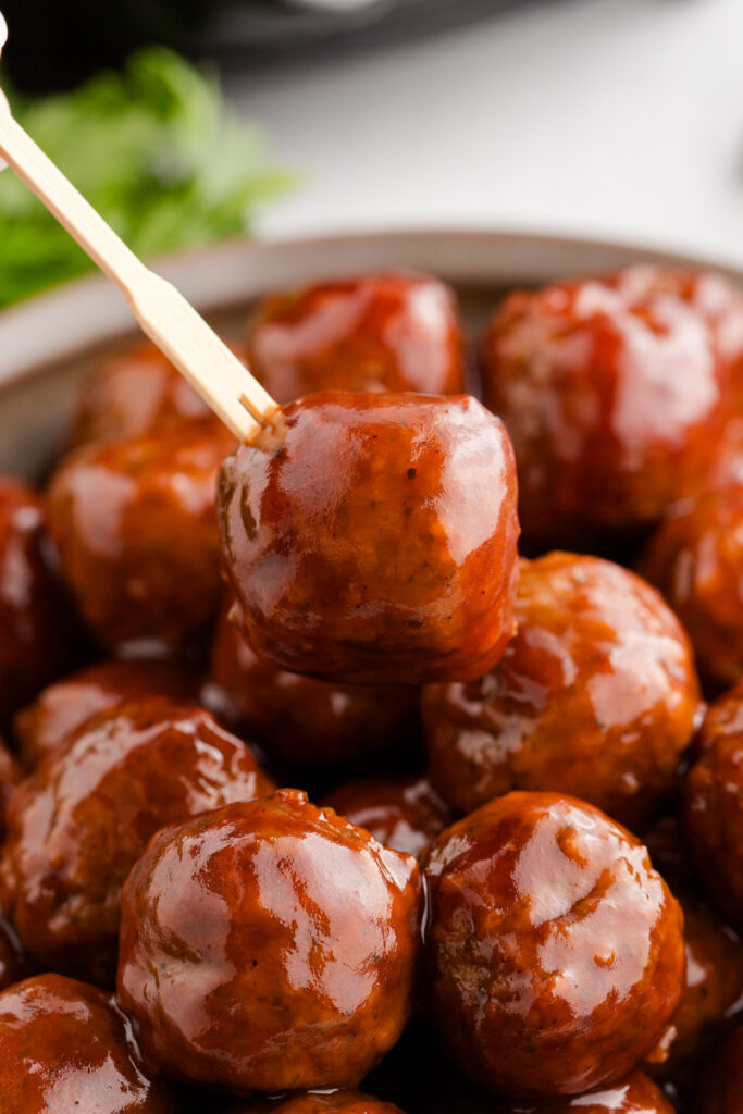 close up image showing a meatball covered in sauce being pulled up by a toothpick