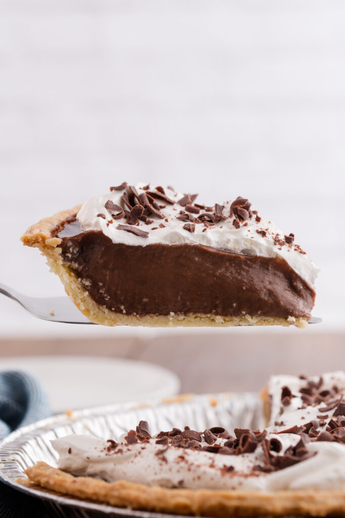 one slice of chocolate pie with cream being pulled from a full pie