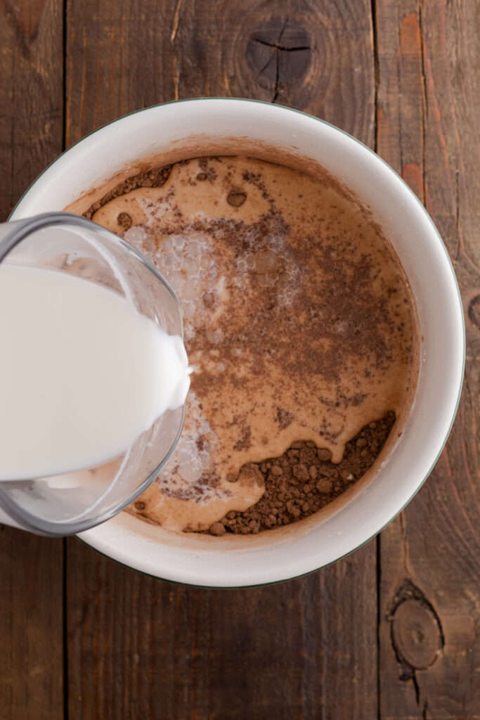 milk being poured into a chocolate mixture inside a white bowl