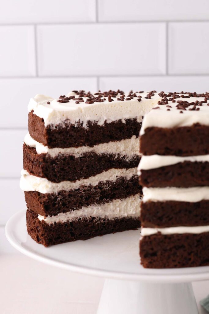 close up image showing 4 layers of chocolate cake with whipped cream in between sitting on a white cake plate