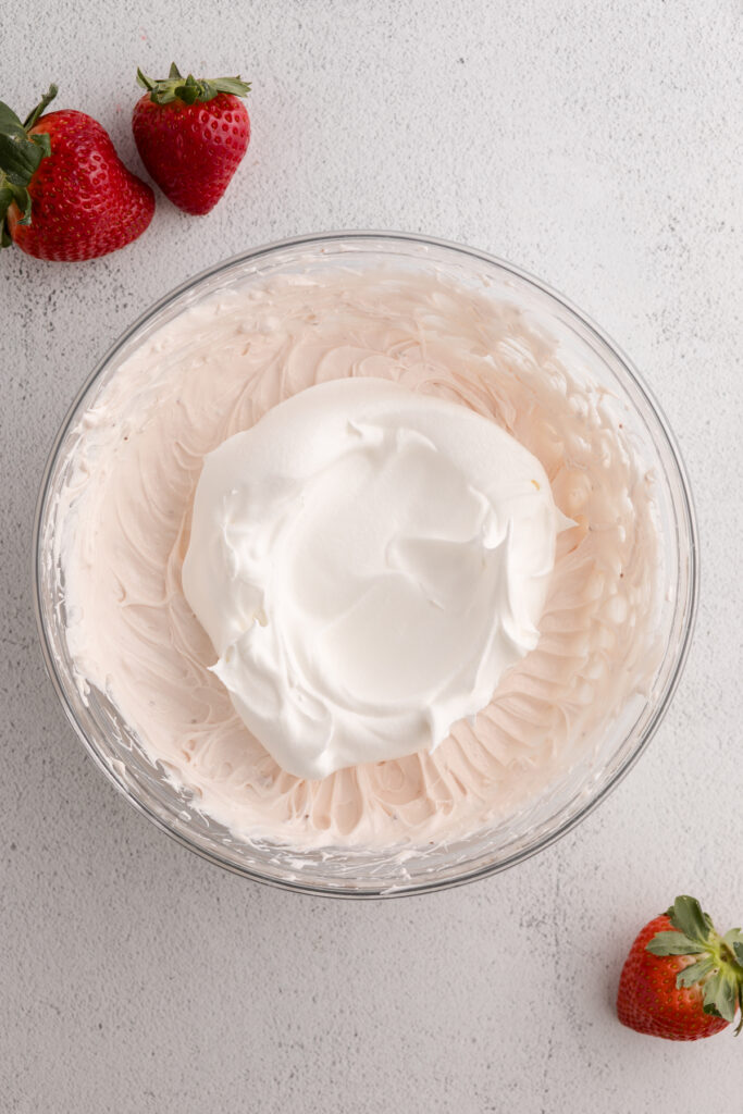 top down image showing a glass bowl with a pink whipped cream cheese and a dollop of cool whip