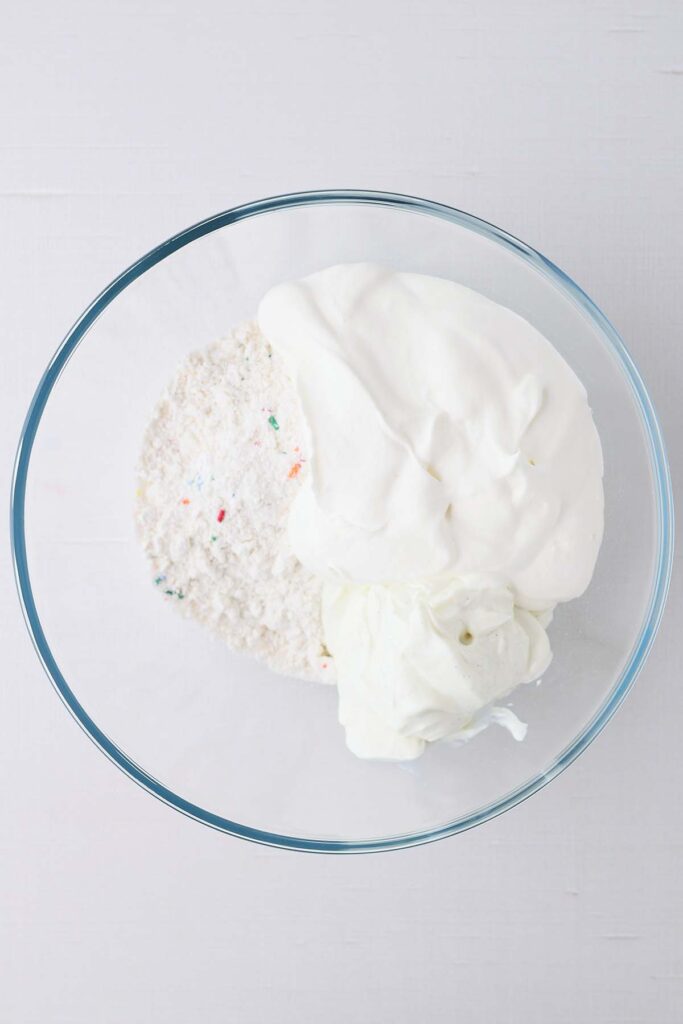 top down image showing a glass bowl filled with cake mix, yogurt, and whipped topping