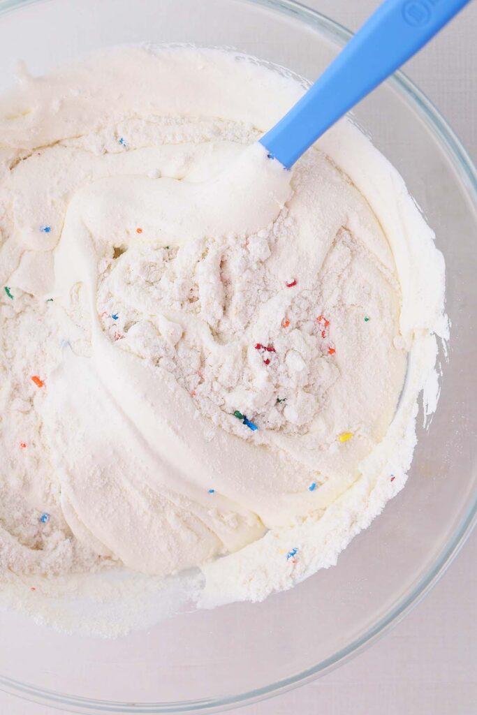 top down image showing cake mix being stirred with a blue spoon with whipped topping