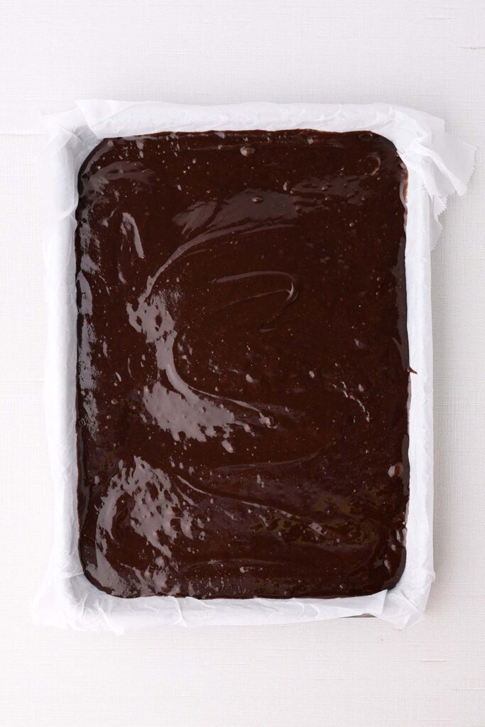 Top down image showing brownie batter in a parchment lined pan