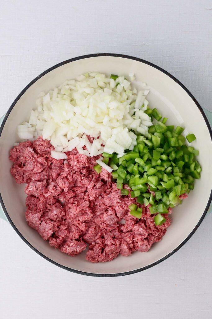 Top down image showing the inside of a pan with uncooked beef, chopped onion, and chopped green pepper
