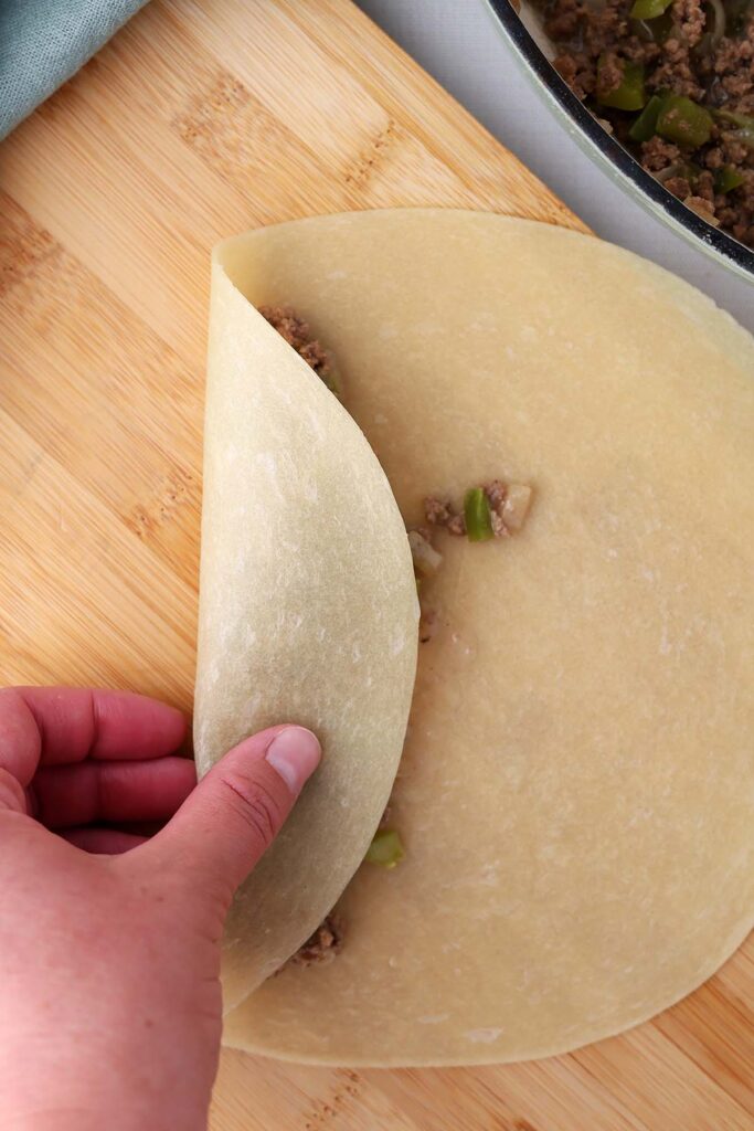 Hand rolling a beef mixture into an uncooked tortilla