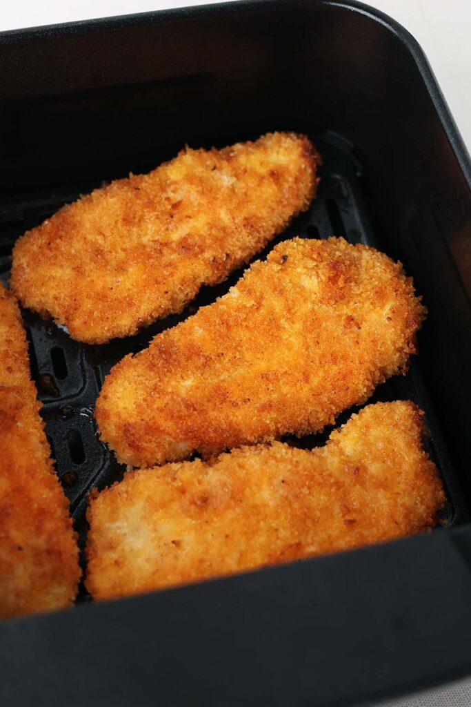 close up image showing four golden crisp tenders sitting inside an air fryer