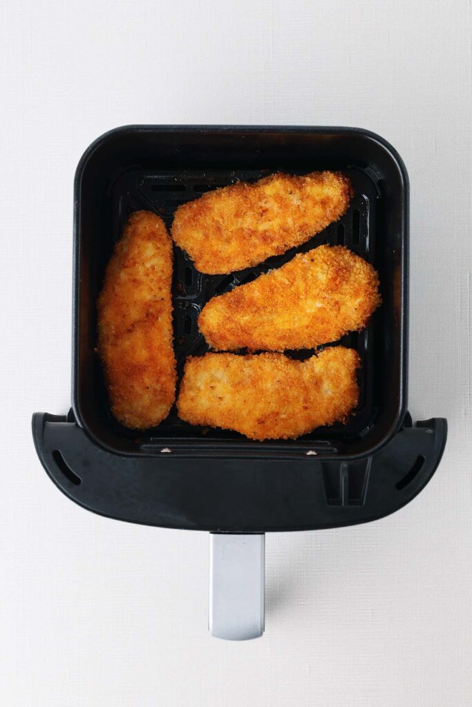 Top down image showing four golden crisp tenders sitting inside an air fryer