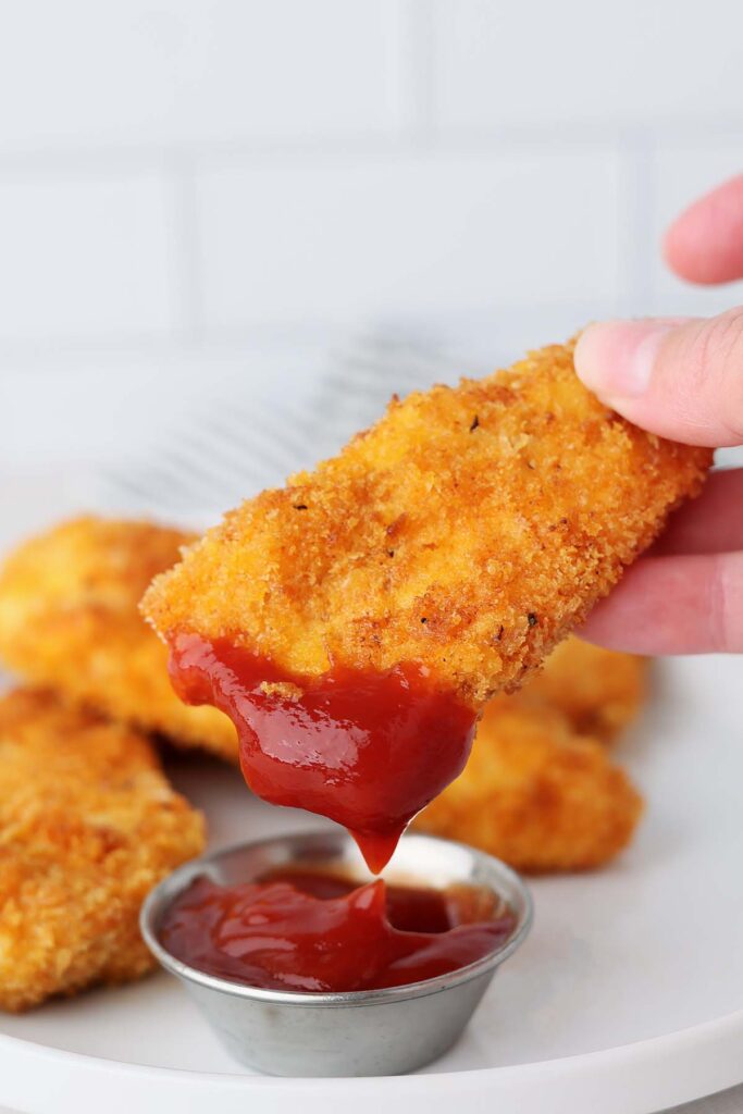 Close up showing a crisp tender being dipped into ketchup