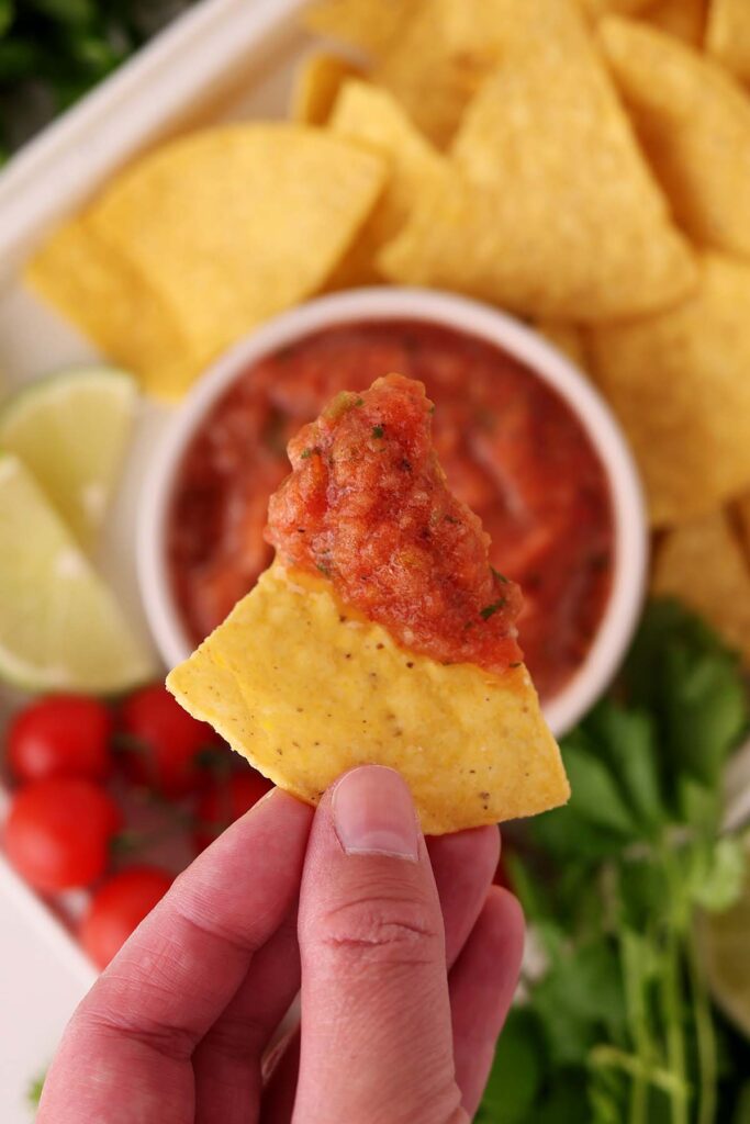 Top down image showing a chip with salsa on the top of it being held by a hand
