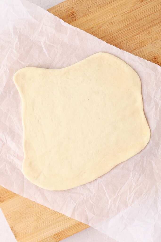 Top down image showing pizza dough rolled out onto a sheet of parchment