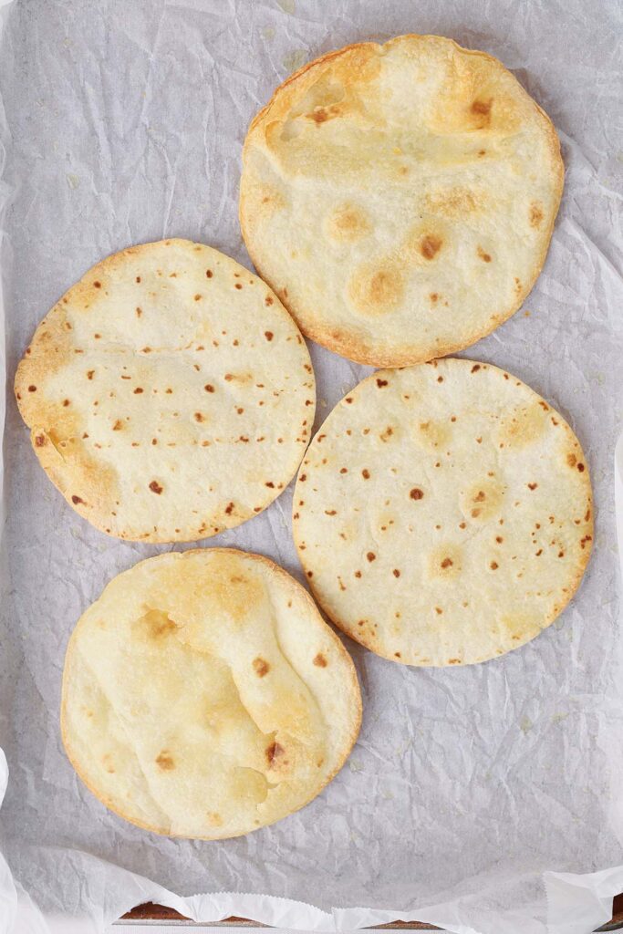 top down image showing four golden crisp tortillas on a white parchment lined tray